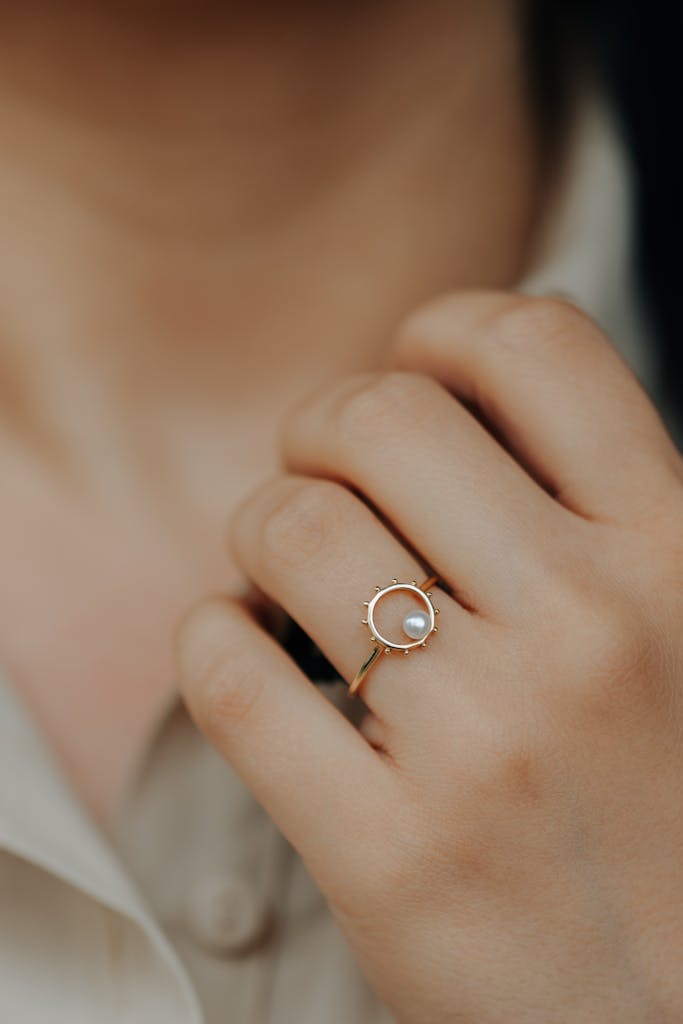 Close-up of a woman wearing a gold ring with a pearl, showcasing elegant jewelry design.